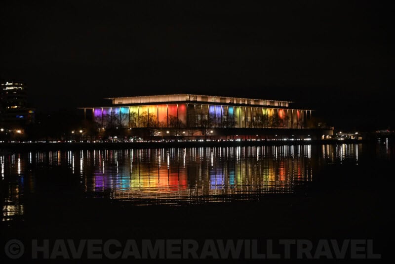 Kennedy Center illuminated in rainbow colors reflected across the Potomac River at night