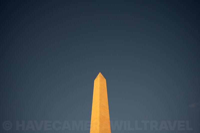 The Washington Monument's pyramidion glowing golden against a dark blue sky