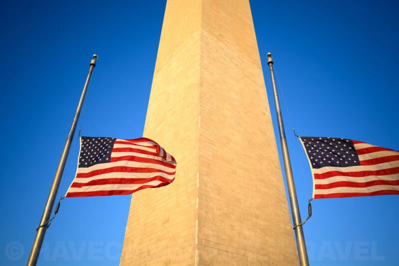 Washington Monument obelisk viewed from below with two American flags flying at half-staff