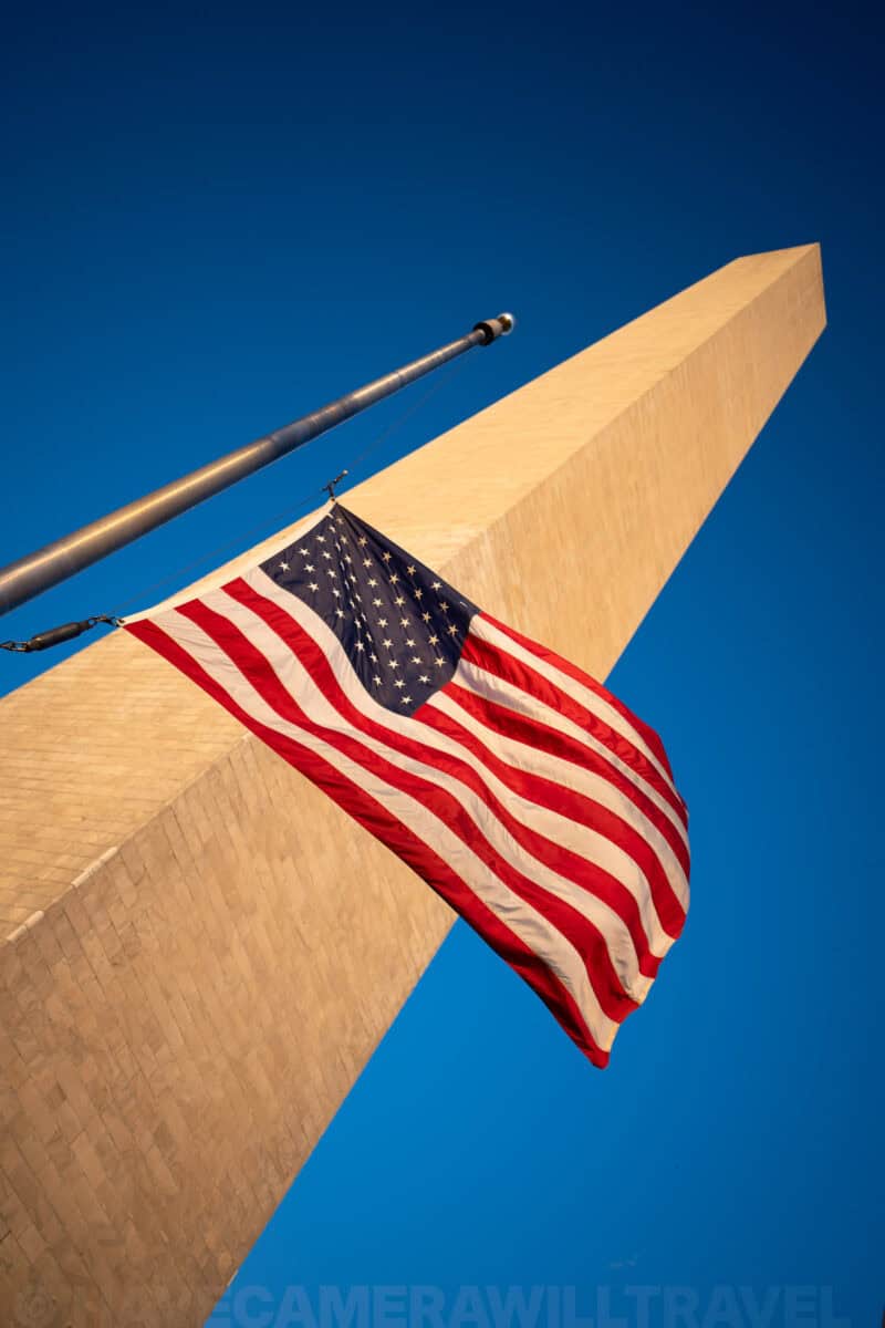 American flag rippling in the wind against the Washington Monument's stone obelisk
