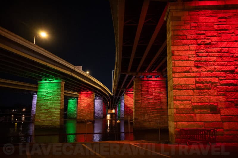 Stone bridge pillars illuminated in red and green beneath overlapping highway overpasses at night