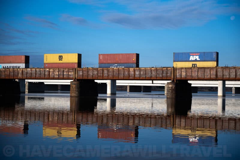 Shipping containers on a rail bridge reflected in still water below