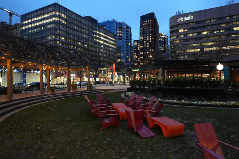 City plaza at dusk with red Adirondack chairs on grass and illuminated office towers behind, ISO 3200 test shot