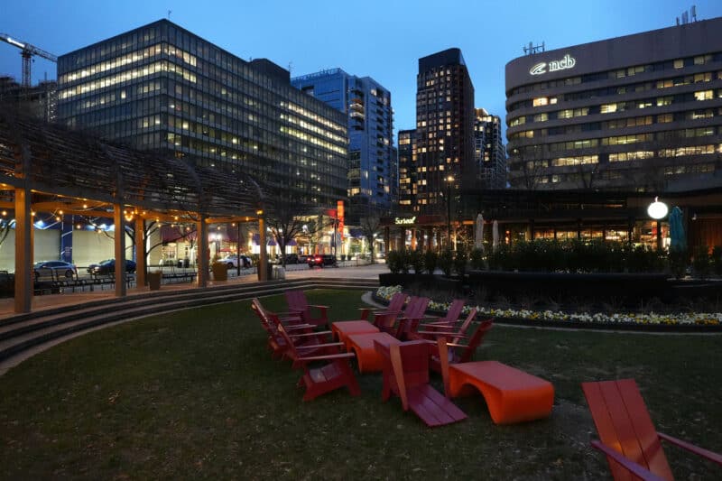Twilight cityscape with red patio chairs on lawn and lit buildings, ISO 6400 sample image