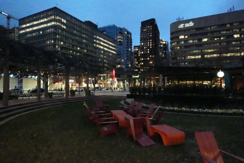 Dark city plaza with red chairs and distant lit buildings, ISO 64000 test shot