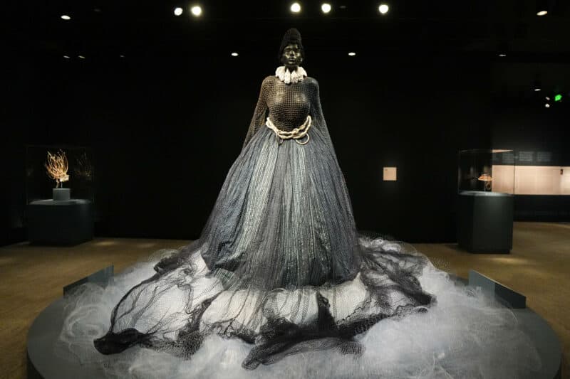 Statuesque figure in a flowing netted gown with a wire train pooling on a museum display platform