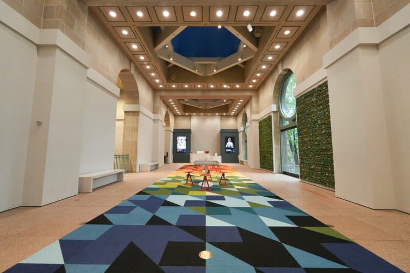 Grand museum hallway with a geometric patterned carpet, arched windows, and a coffered skylight ceiling