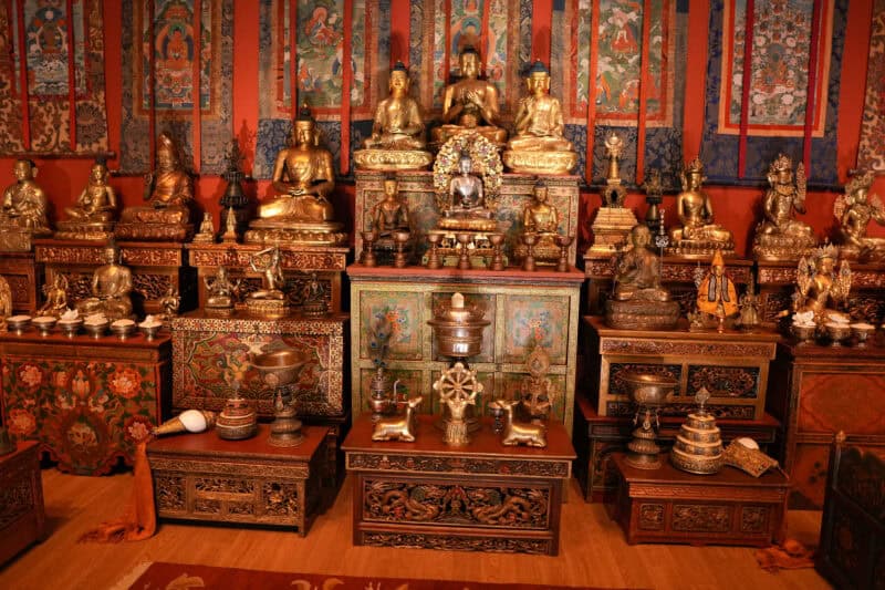 Tibetan Buddhist shrine room crowded with gilded Buddha statues and painted thangka scrolls