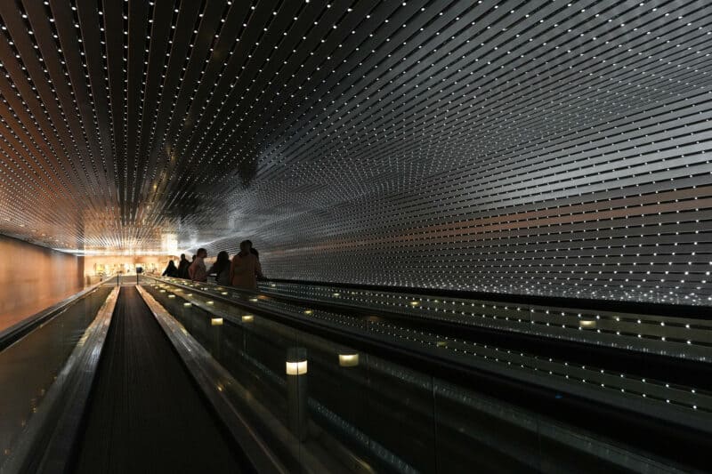 Museum visitors riding a long illuminated moving walkway lined with thousands of small lights
