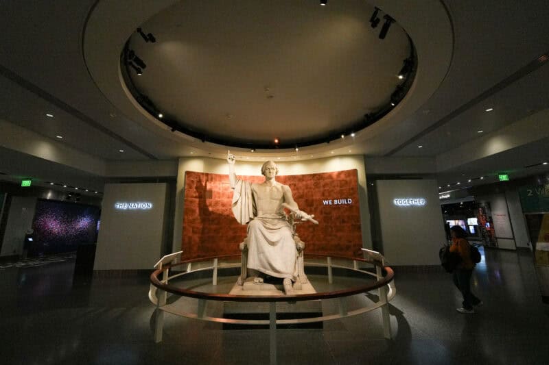 Classical marble statue of a seated robed figure lit beneath a circular skylight in a museum atrium