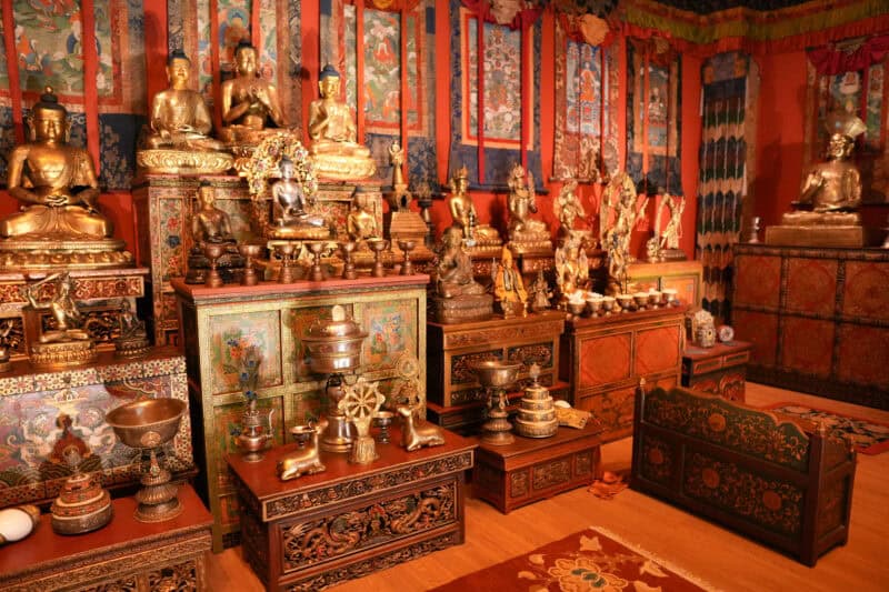 Tibetan Buddhist altar room filled with rows of bronze Buddha statues and ornate painted cabinets