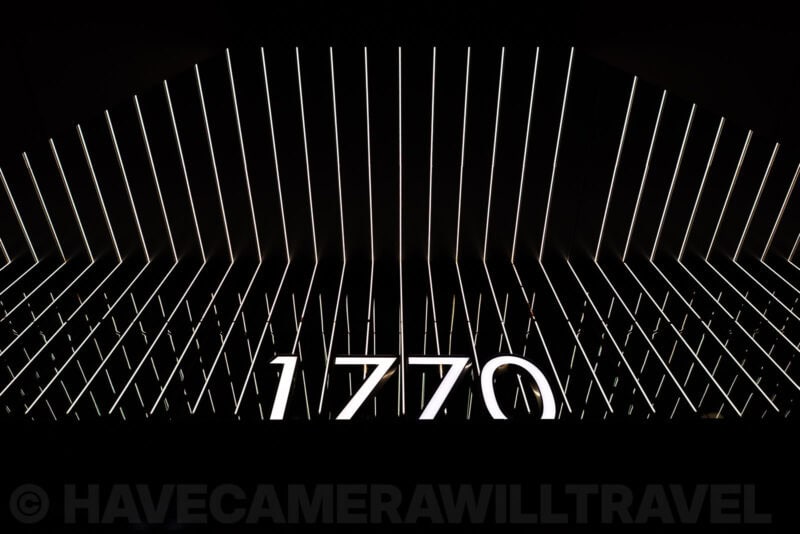 Illuminated '1770' sign framed by radiating white light bars in a dark exhibit