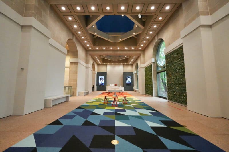 Museum atrium corridor with a colorful geometric carpet runner and arched glass windows