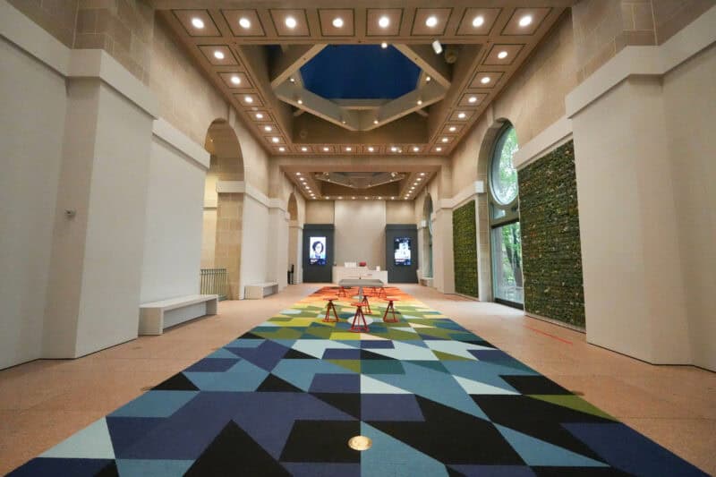 Museum atrium hallway with a vivid geometric carpet pattern beneath a skylit coffered ceiling