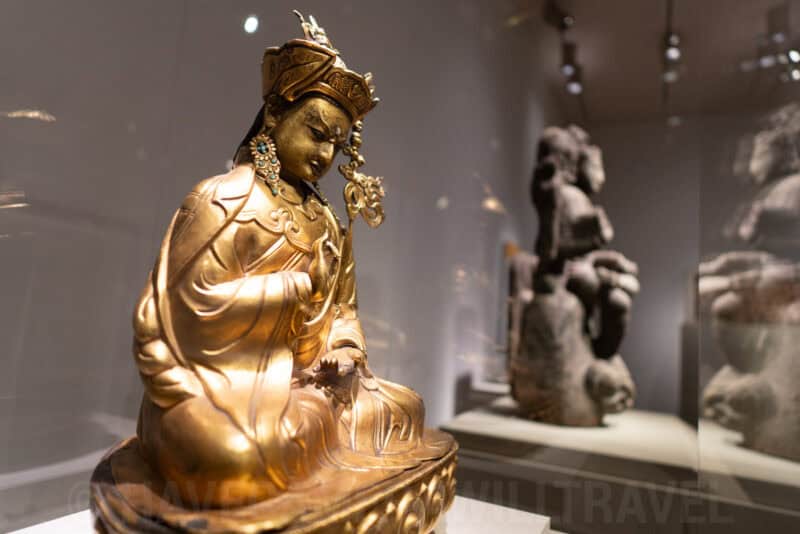 Close-up of a gilded Buddhist deity statue with ornate crown in a museum case