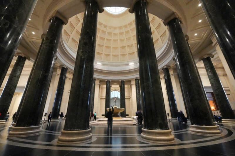 Grand domed rotunda with tall dark marble columns encircling a central fountain sculpture