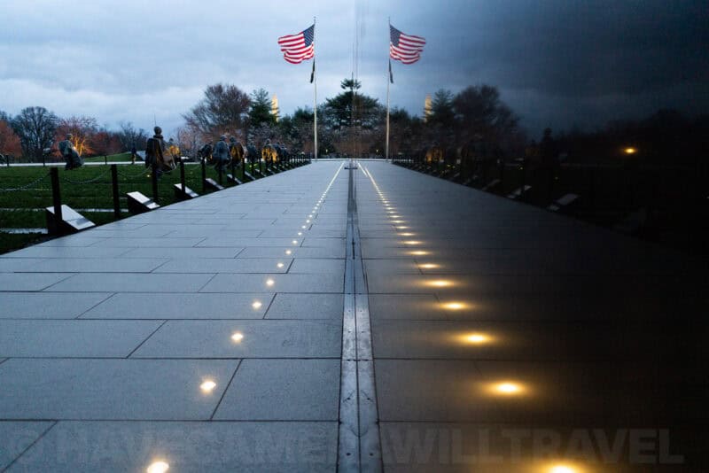 Vietnam Veterans Memorial wall reflecting American flags and statues at dusk