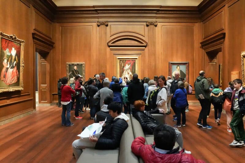 Crowd of museum visitors viewing framed royal portraits in a wood-paneled gallery