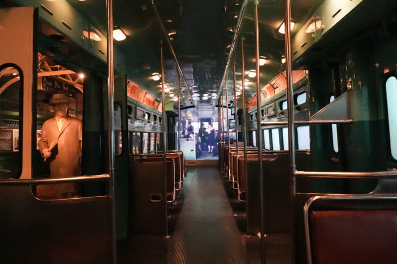 Interior of a vintage streetcar exhibit with rows of seats and a mannequin figure by the door