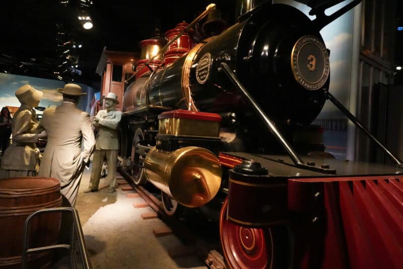 Close-up of a vintage steam locomotive replica with mannequins in period dress nearby