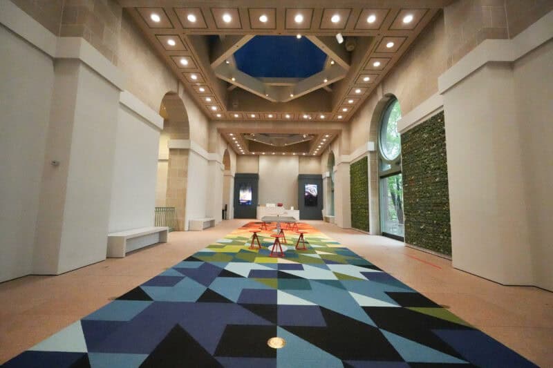 Museum hallway with a bold geometric carpet design and arched windows under a skylight