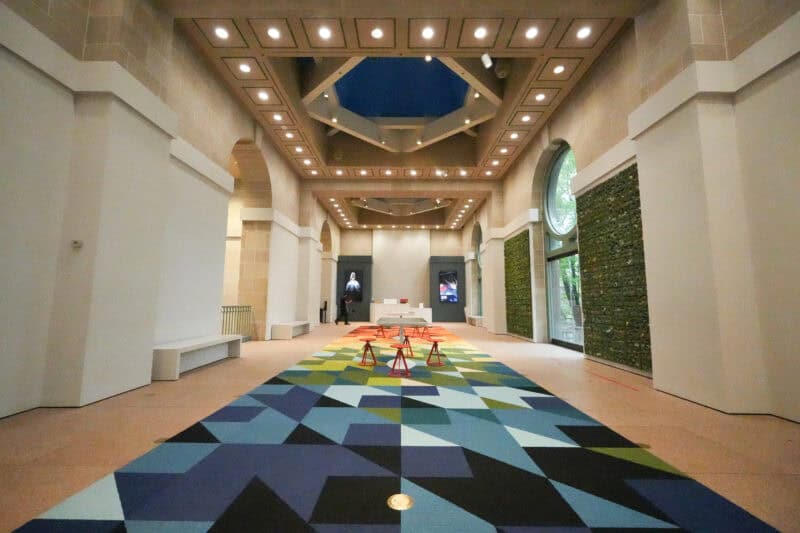 Museum atrium corridor with a colorful triangular carpet pattern and arched glass windows