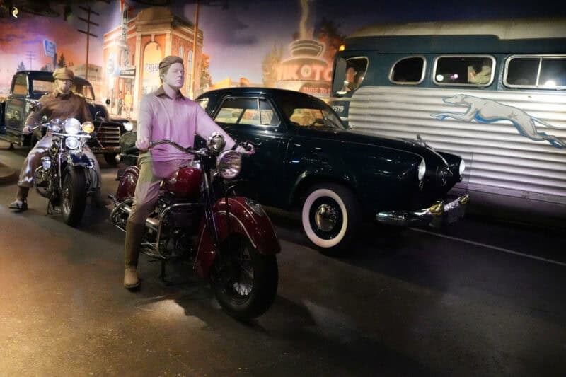 Vintage roadside scene diorama with mannequins on motorcycles beside a classic car and bus
