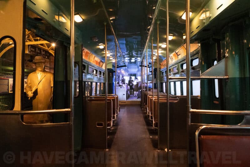Interior of a vintage streetcar exhibit with a mannequin passenger and wooden seats