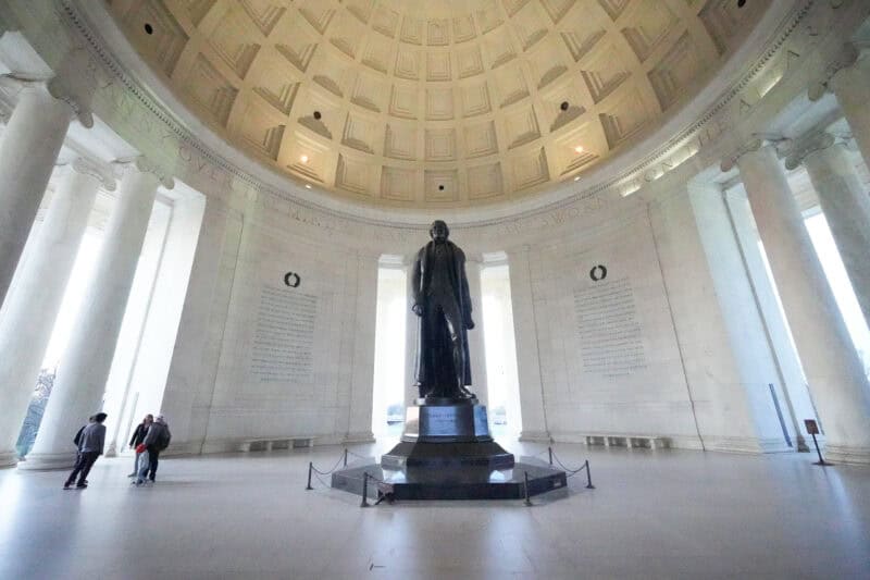 Bronze statue of Thomas Jefferson standing beneath the tall domed ceiling of his memorial