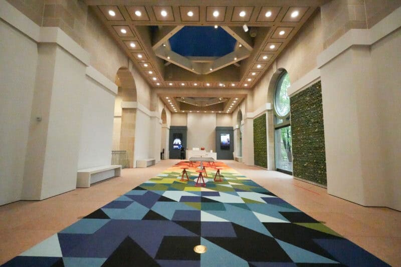 Bright museum hallway with a colorful geometric carpet and arched windows under a skylight