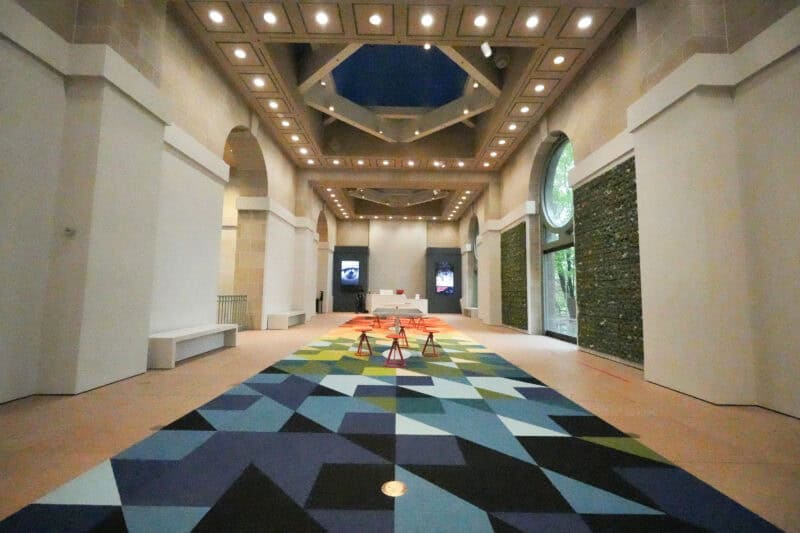 Museum hallway with a geometric carpet pattern and arched glass windows along the walls