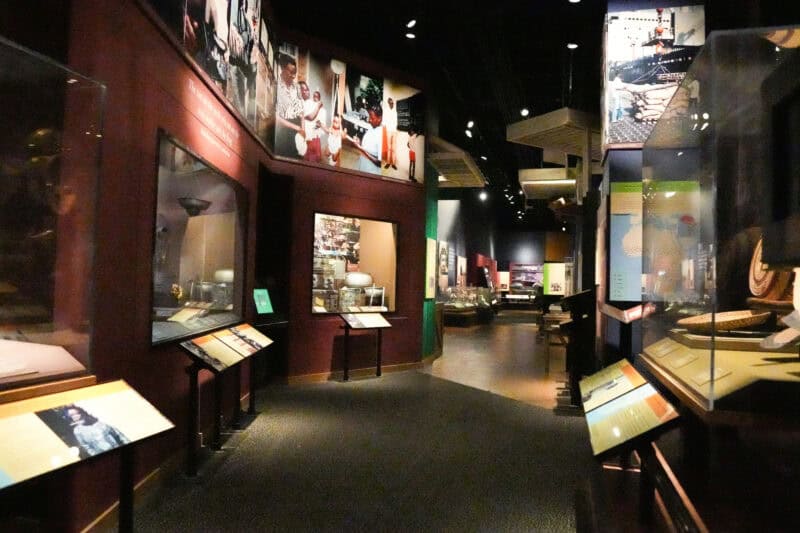 Museum exhibit corridor with illuminated wall panels and rows of glass display cases