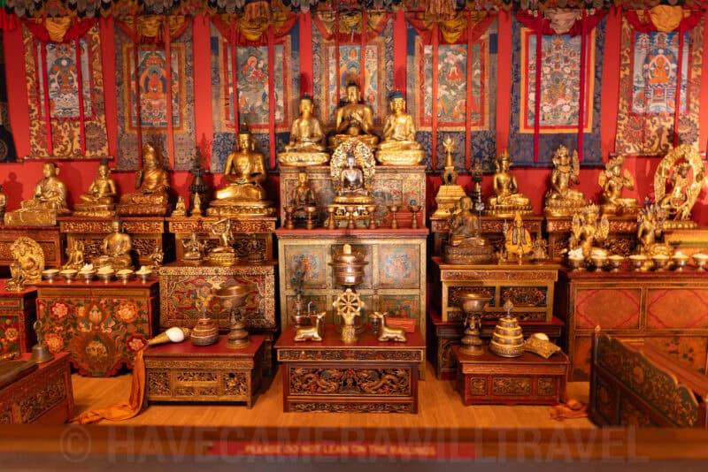 Golden Buddhist statues and thangka banners displayed in a museum shrine room