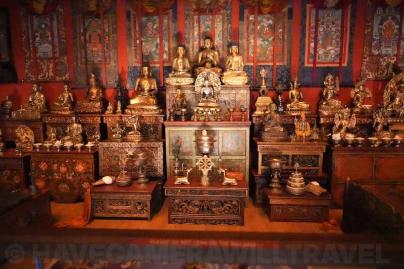 Tibetan Buddhist altar room crowded with bronze statues and painted thangka wall hangings