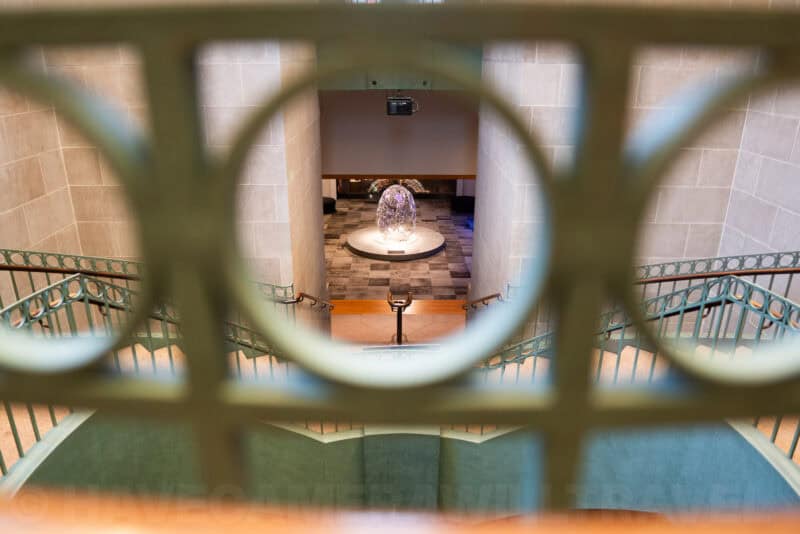 View through a circular railing opening down a staircase to a sculpture display