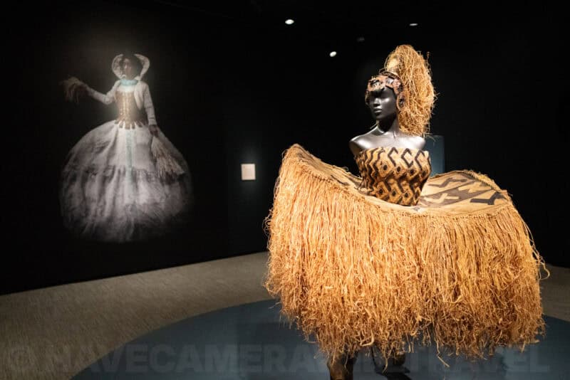 Museum mannequin in a raffia grass skirt costume beside a projected historical portrait