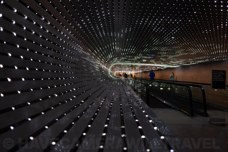 Illuminated tunnel walkway with sparkling light patterns and visitors walking through
