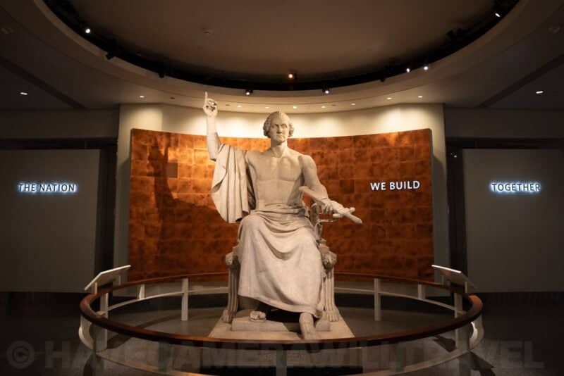 Large marble statue of George Washington seated beneath illuminated museum text panels