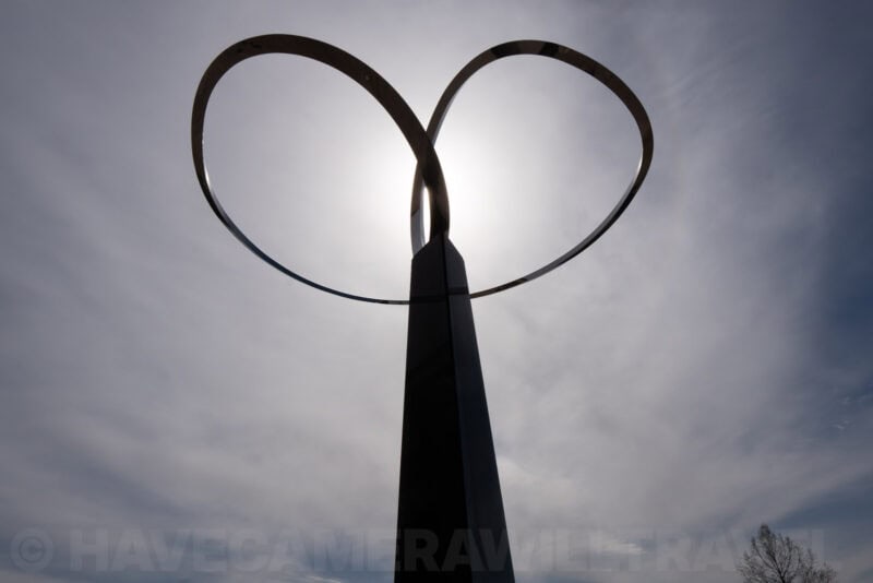 Silhouetted heart-shaped metal sculpture backlit by the sun against a cloudy sky