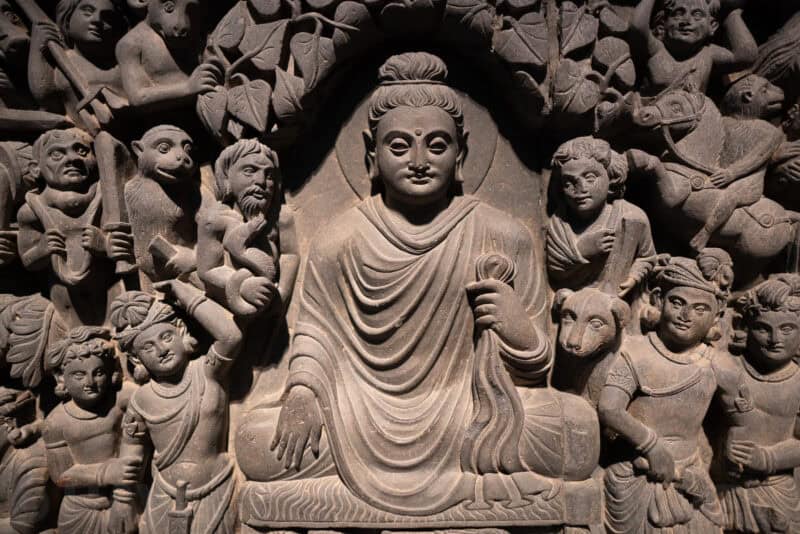 Carved stone relief depicting a seated Buddha surrounded by figures and animals