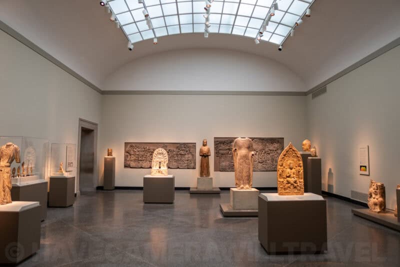 Museum gallery with ancient carved stone sculptures displayed under a skylight
