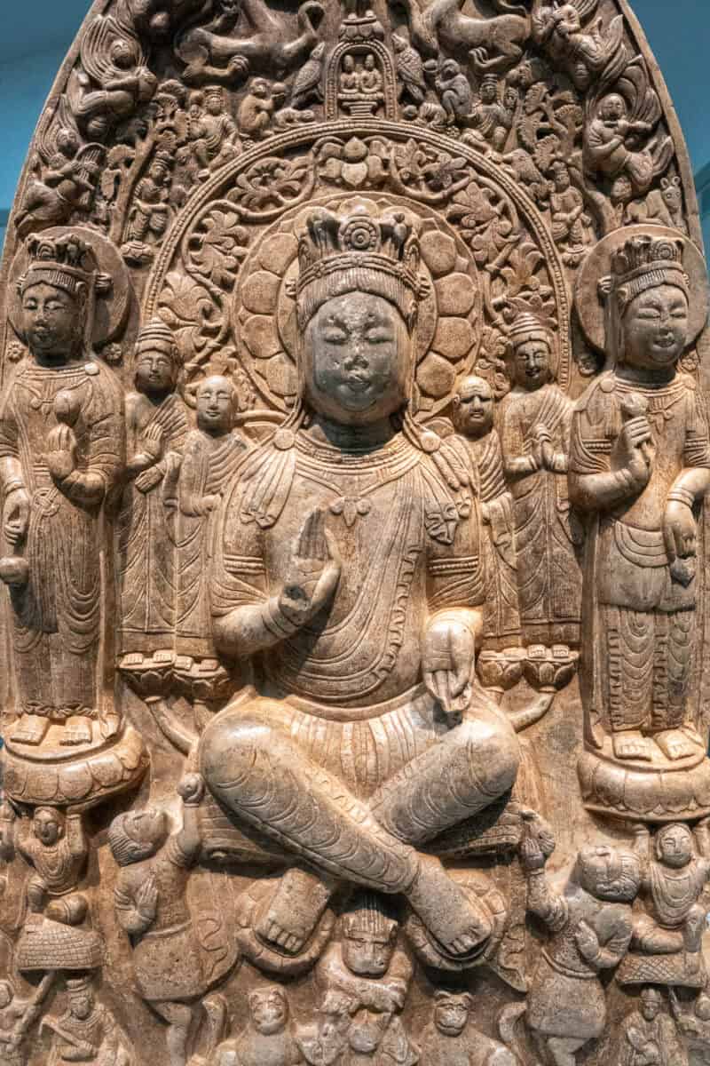 Ancient carved stone relief of Buddhist figures with surrounding attendants
