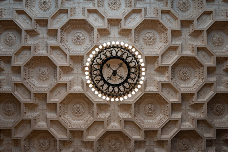 Ornate coffered ceiling with a circular chandelier of bare bulbs, viewed from below