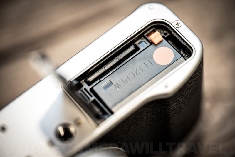 Open battery compartment of the Fujifilm X100 series showing the SD card slot fitted snugly beside the battery