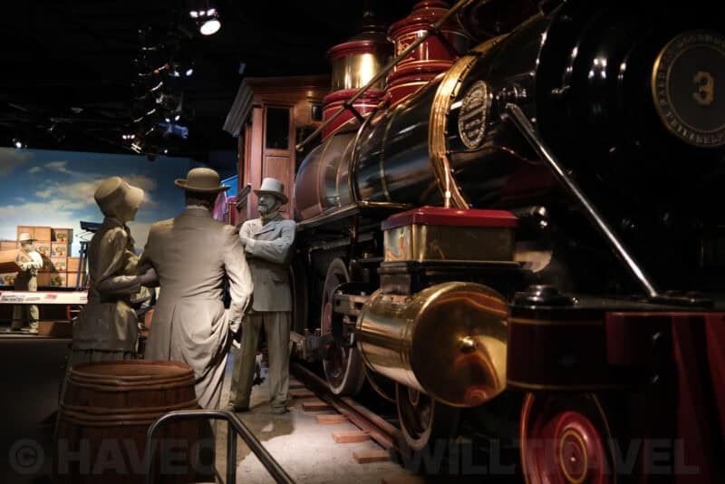 Life-size figures beside a vintage steam locomotive in a museum diorama at ISO 125 with minimal noise