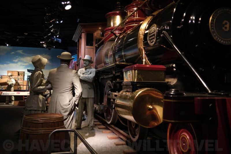 Life-size figures beside a vintage steam locomotive in a museum diorama at ISO 200 with clean tones