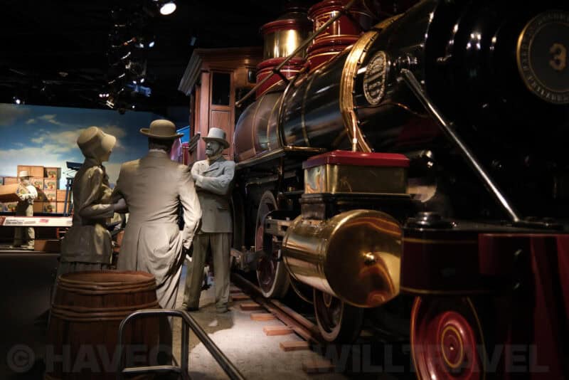 Life-size figures beside a vintage steam locomotive in a museum diorama at ISO 250 with faint grain