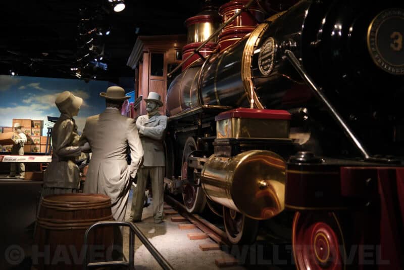 Life-size figures beside a vintage steam locomotive in a museum diorama at ISO 320 with light noise in shadows
