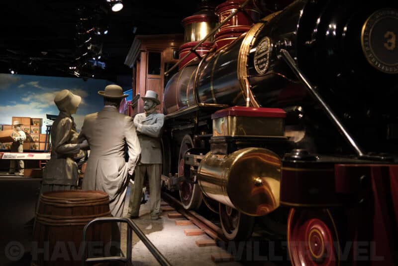 Life-size figures beside a vintage steam locomotive in a museum diorama at ISO 500 with mild noise texture
