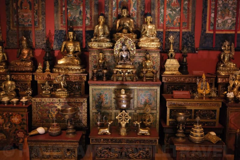 Gilded Buddhist statues and shrine display in a museum exhibit at ISO 12800 showing pronounced grain